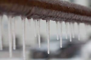 Icicles hanging from a brown pipe. Frozen water and metal surface, winter time concept. selective focus shallow depth of field